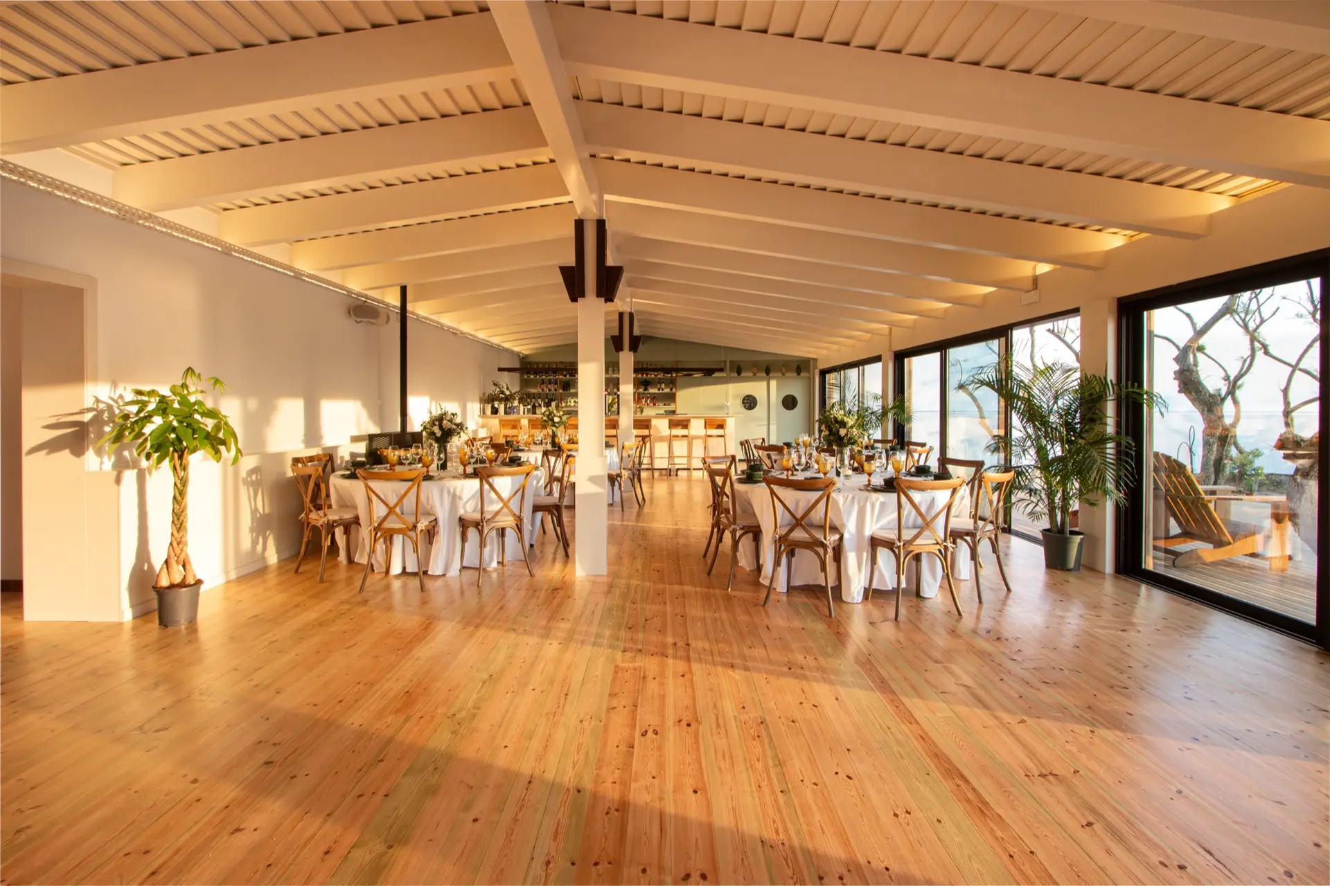 Interior da Cavalariça, uma sala de madeira clara com grandes vidraças e mesas redondas postas