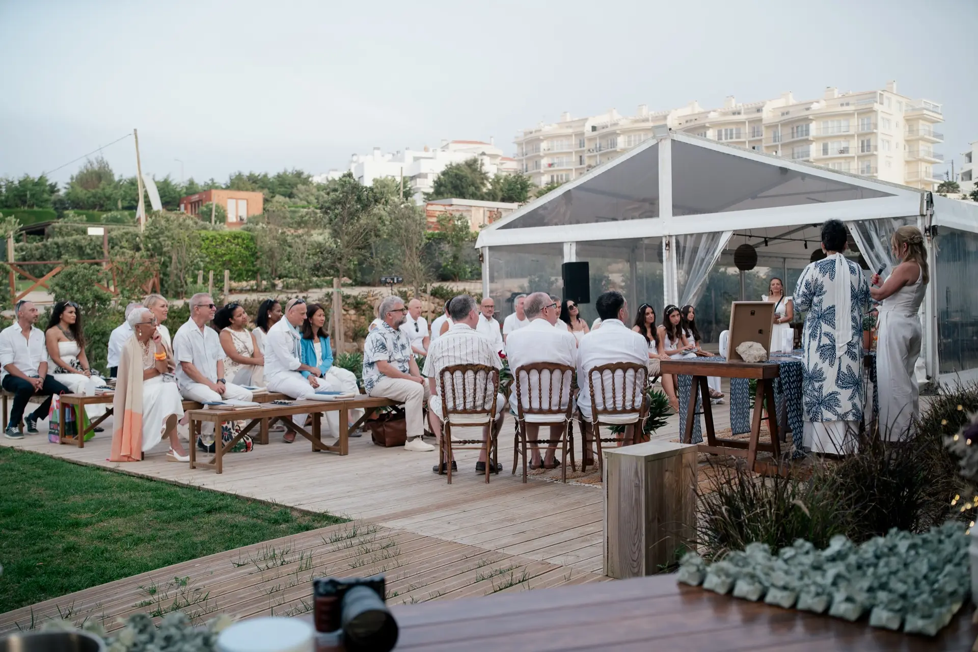 Convidados vestidos de branco numa cerimónia no deck, junto ao relvado