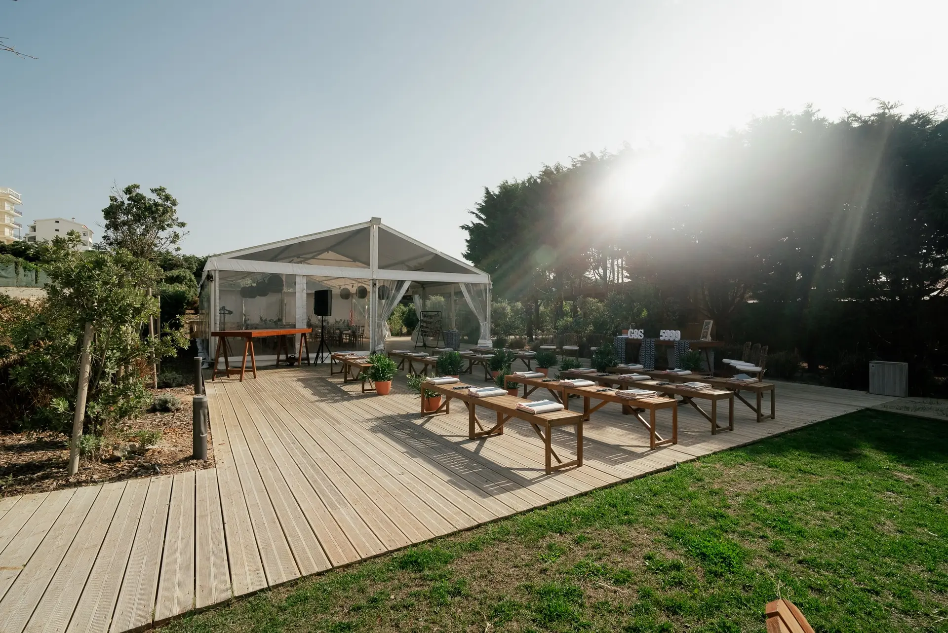 Bancos de madeira alinhados no deck para uma cerimónia, com a tenda ao fundo e o sol a entrar