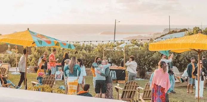 Festa no relvado do La Barraque com guarda-sóis coloridos e o mar ao fundo