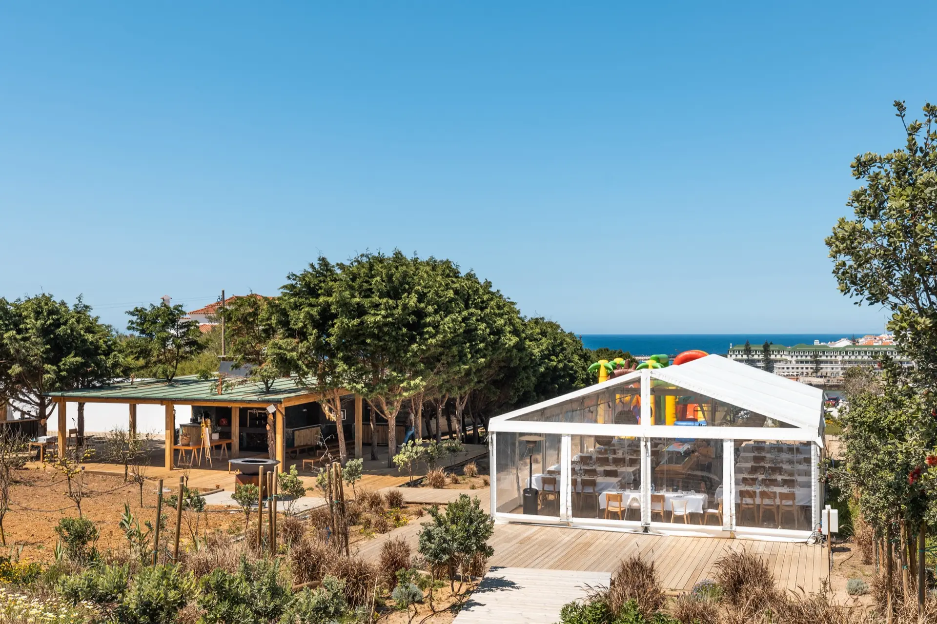 A tenda branca vista de cima, rodeada de jardim, com o mar ao fundo